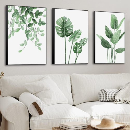 a tryptic of green and white plant images hanging on a wall above a sofa
