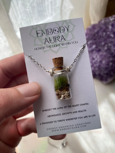 a hand holding a card with a terrarium in a bottle necklace